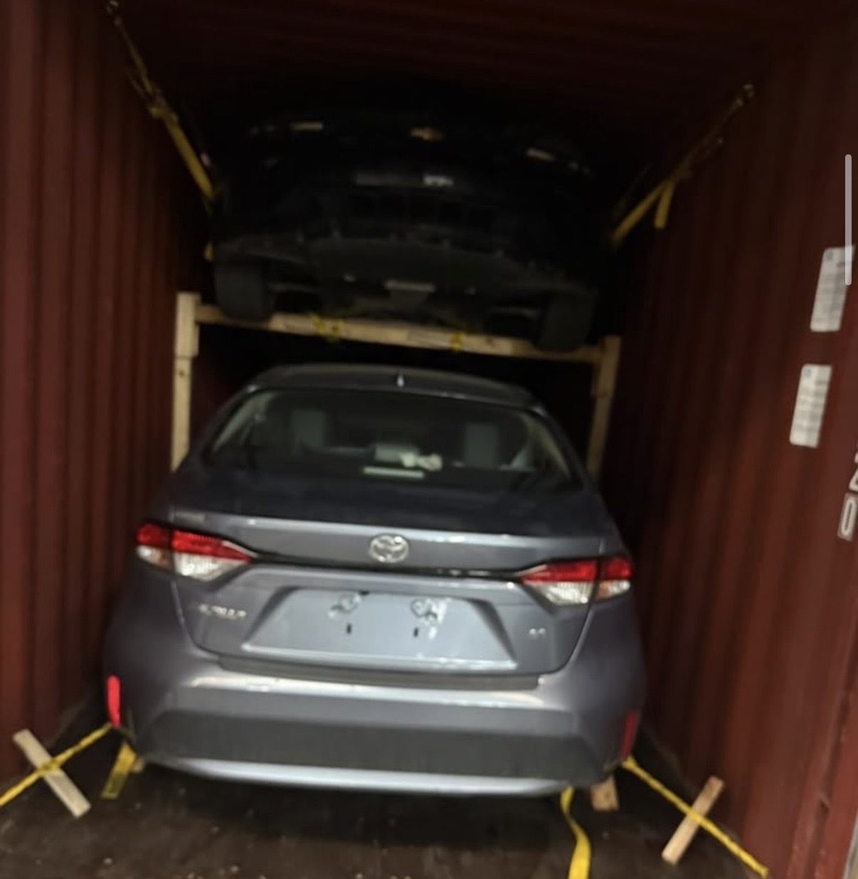 Camaro negro colocado en la parte superior de un contenedor de exportación, con un Toyota Corolla debajo, rumbo a Paraguay